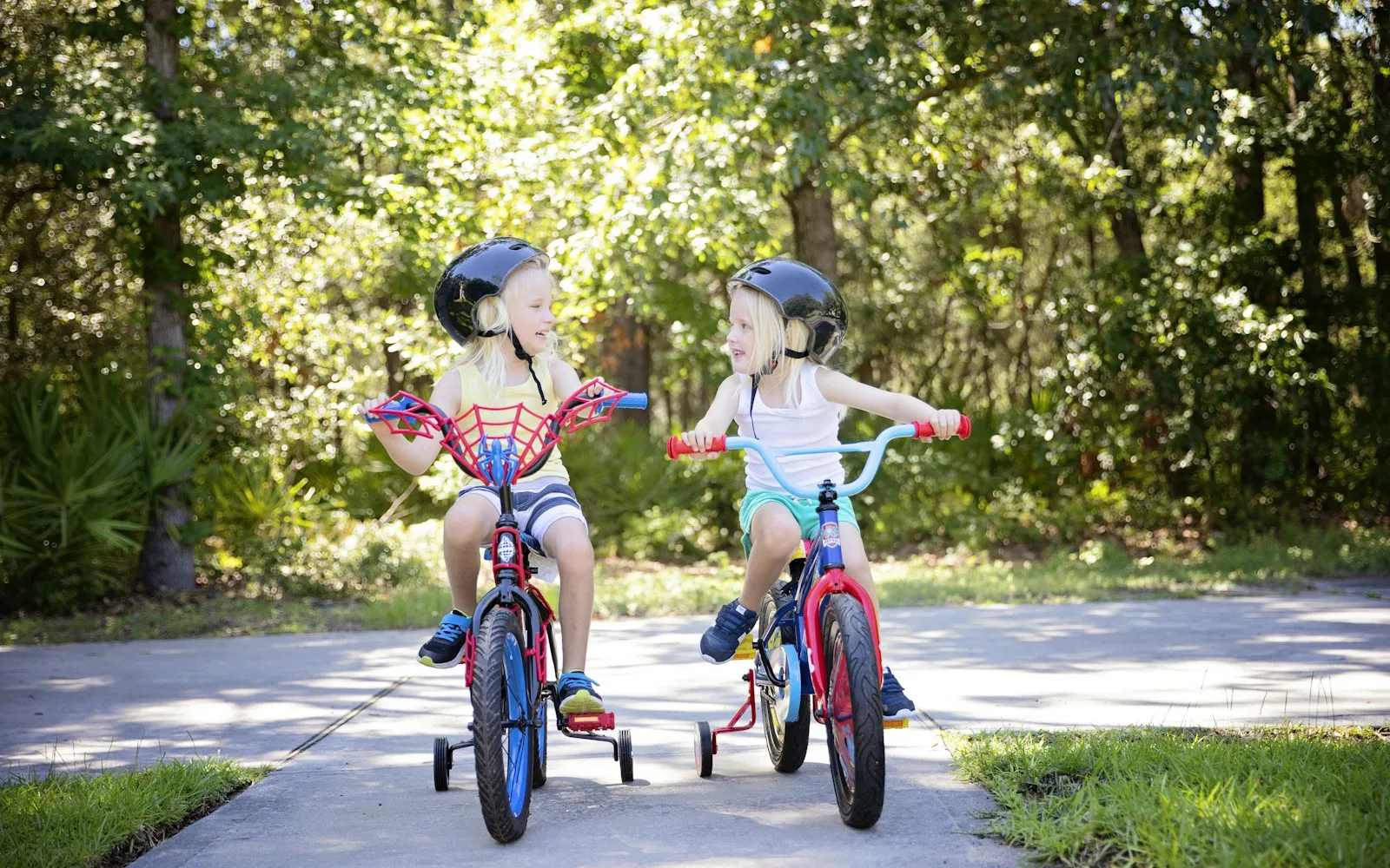 Two children in helmets riding small pedal bikes with training wheels
